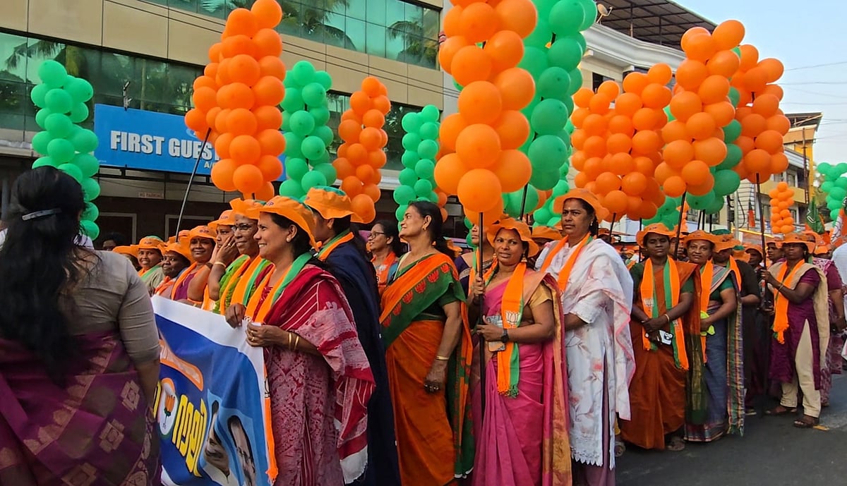 Group of women wearing orange caps and scarves at a BJP campaign rally in Guruvayur, holding orange and green balloons and party flags.