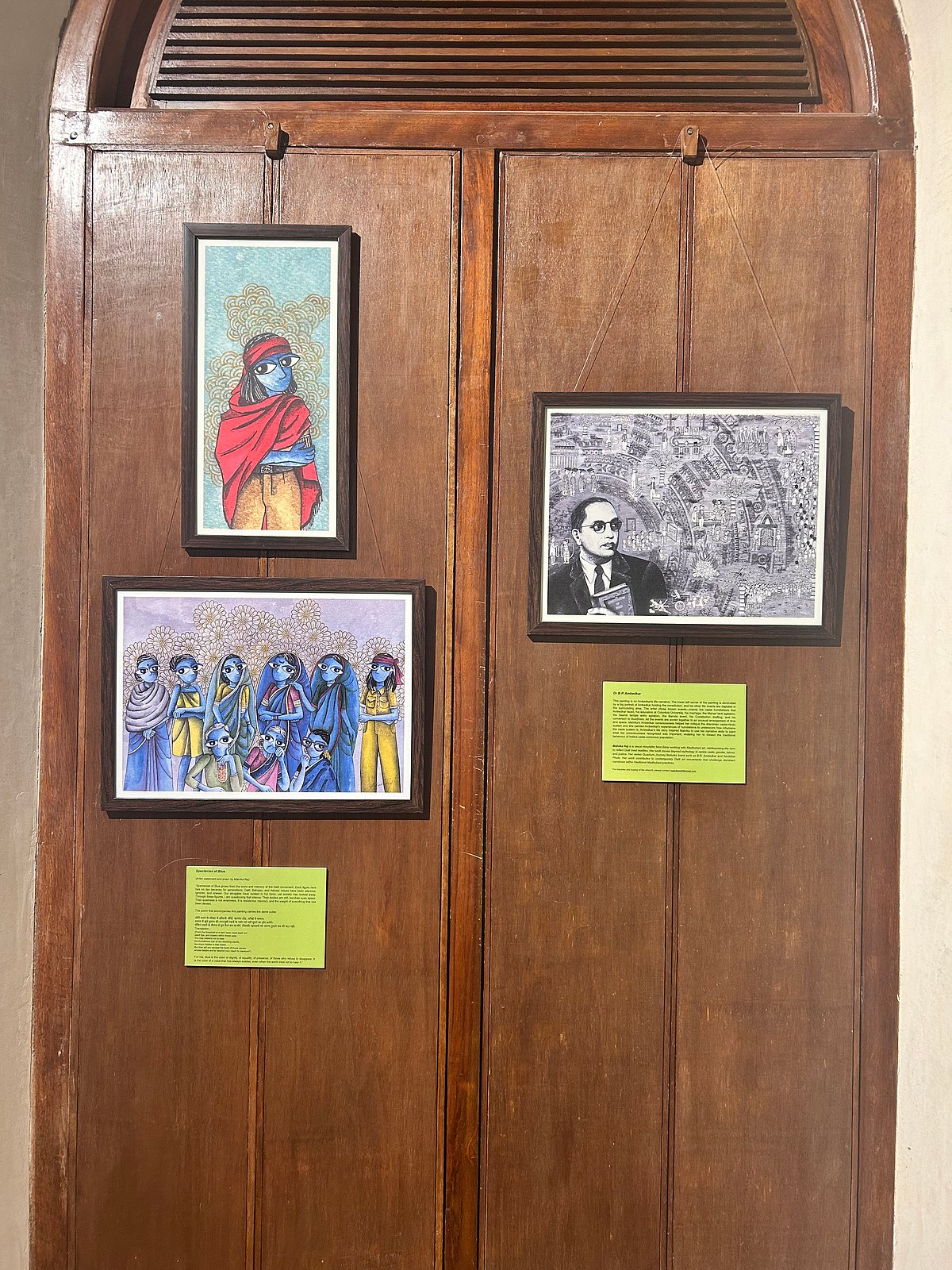Framed artworks displayed on a wooden panel, including a portrait of BR Ambedkar and illustrations of people, exhibited as part of the Building Begumpura conference in Bengaluru.