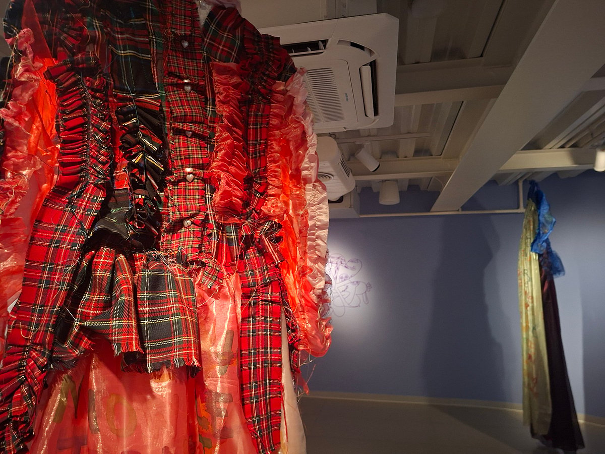 Close-up of a textile garment featuring red tartan fabric, ruffles, and visible stitching details.