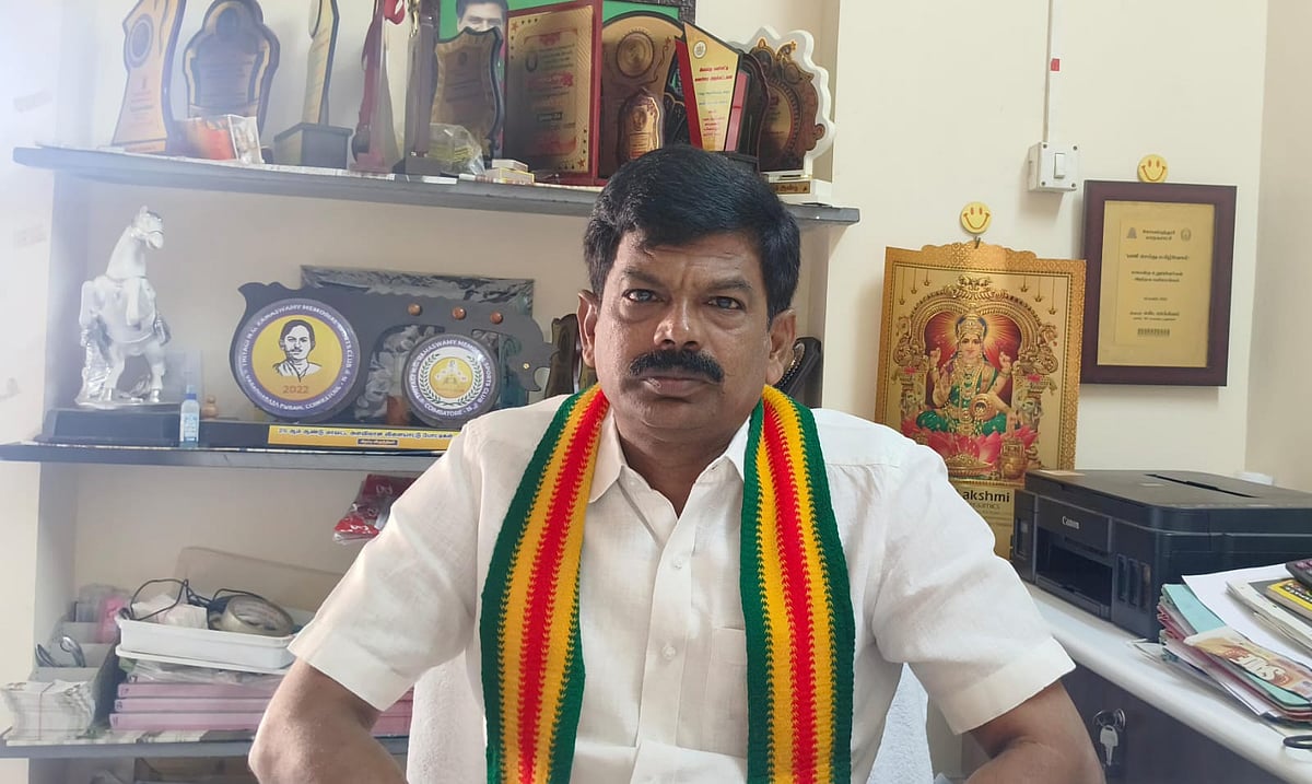 KS Dhanapal in a white shirt and green, yellow and red scarf