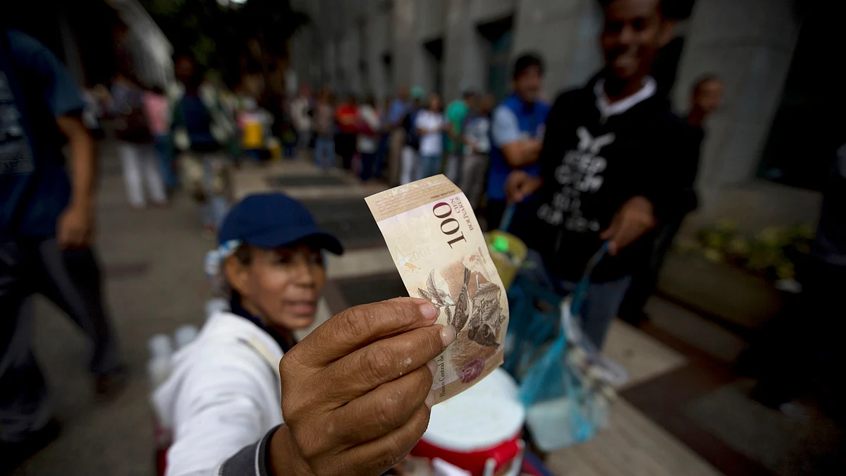 A street vendor inspects the authenticity of a 100-bolivar note as people stand in line outside a bank to deposit their bank 100-bolivar bank notes, in Caracas, Venezuela, Tuesday, Dec. 13, 2016 (AP Photo/Fernando Llano)