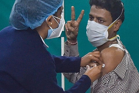 A female health professional administers the first dose of COVID-19 vaccine to a man who is seen showing the victory sign hand gesture.