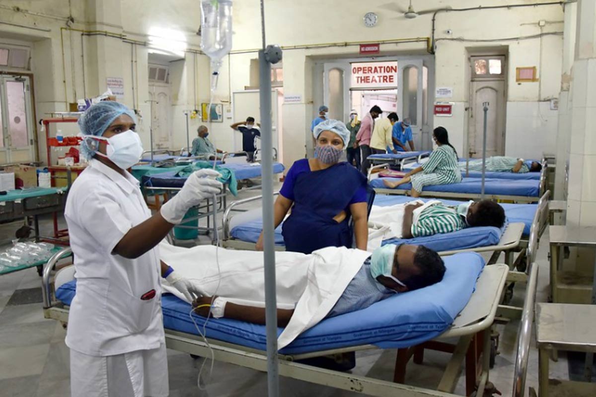 Patients lie in a ward, as healthcare workers attend to a male patient, as a nurse looks at the IV line