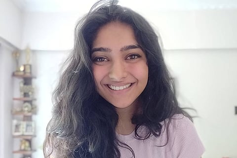 Karthika Muralidharan is seen wearing a pink tee and is seen smiling at the camera in the image. 