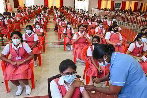 Students sitting in an auditorium in uniform as a healthcare worker vaccinates a student