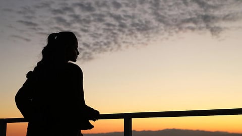 Silhouette of a woman standing near a railing staring into the sunset