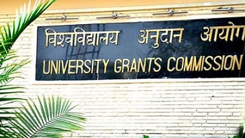 The name board of the UGC on a white, exposed-brick wall. The name board is black granite, and the expansion of UGC is given in golden letters in both Hindi and English.