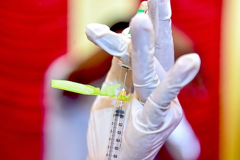 A gloved hand uses a syringe to draw COVID-19 vaccine from a vial 