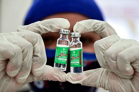 Two vials of covishield are shown to the camera by a healthcare worker wearing gloved hands