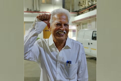 Poet-activist Varavara Rao in a white shirt, smiling with his right hand raised