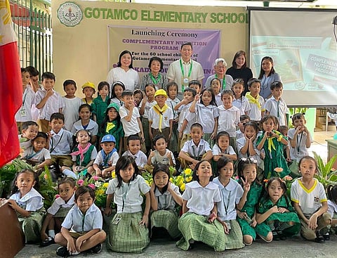 Grade schoolers of Gotamco Elementary School pose for a photo with Okada Foundation President James Lorenzana, Kabisig ng Kalahi Founder Vicky Wieneke, and other guests at the launching ceremony of Complementary Nutrition Program.