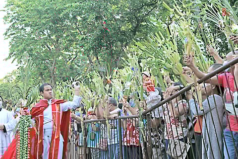 Catholic faithful raise their palm fronds outside the Baclaran Church to have them blessed by a priest. At right, a young girl weaves palm leaves at Sacred Parish in Quezon City on 22 March.