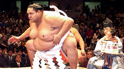 (FILES) This file photo taken on 29 September 2001 shows Hawaiian-born former sumo grand champion Akebono, performing his last ring entrance ceremony before a hair cutting ceremony to mark his official retirement from professional sumo, at the Kokugikan stadium in Tokyo, while a sumo referee holds his son Hiroshi (R). Akebono, the first foreign-born sumo wrestler to become a "yokozuna" or grand champion, died at the age of 54 after struggling with heart failure, officials and media said on 11 April 2024.
