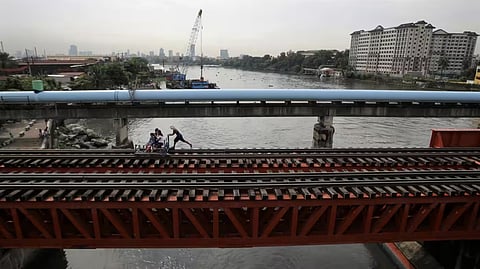 A man pushes a hand cart equipped with benches as he ferries passengers along a railway in Manila.  