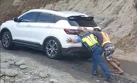 Pushing Duo: A Tuba Police officer and a volunteer assist an SUV driver in maneuvering his vehicle through a rugged portion of Kennon Road in Tuba, Benguet.
