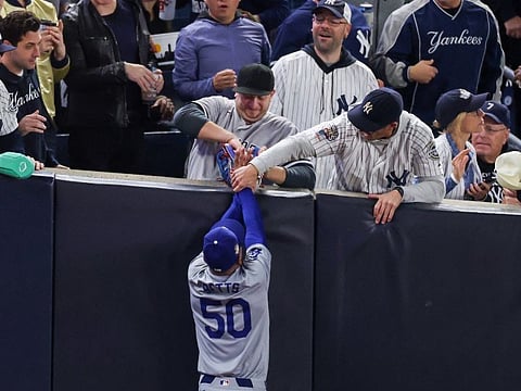 Fans Austin Capobianco (L) and John Peter (R) interfere with Mookie Betts #50 of the Los Angeles Dodgers as he attempts to catch a fly ball in foul territory during the first inning of Game Four of the 2024 World Series.
