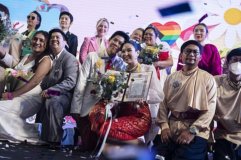 A same-sex couple (C) poses for pictures at a marriage registration event at Paragon shopping mall in Bangkok on 23 January 2025. A high-profile gay couple married in Thailand on 23 January as the kingdom's same-sex marriage law went into effect, an AFP journalist saw, among the first of hundreds expected to do so.