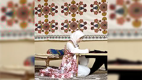 A young girl doing hand embroidery. A sample could be seen at the background