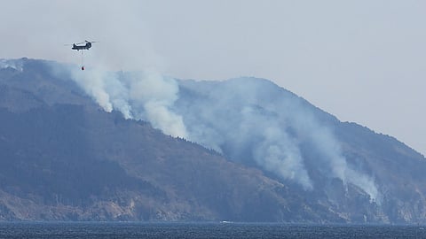 A helicopter is pictured as smoke rises due to a wildfire on a mountainside near the city of Ofunato, Iwate Prefecture on 28 February 2025. 