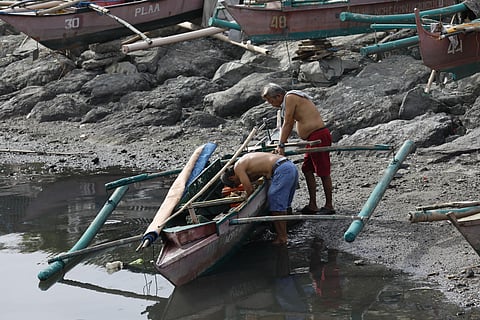 Fisherfolk repair their boat along the shores of Manila Bay, preparing for their next journey at sea. A Supreme Court ruling that allows commercial fishing in municipal waters is impacting the livelihood of fishermen nationwide.