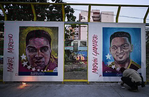 A man lights a candle in front of paintings of Venezuelan migrants deported from the US to a maximum security prison in El Salvador during a vigil in front of El Salvador embassy in Caracas on 2 April 2025.