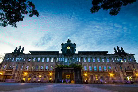The University of Santo Tomas Main Building at dusk, illuminated by warm lights under a blue evening sky, known as Asia’s first earthquake-resistant building and a landmark of academic heritage.