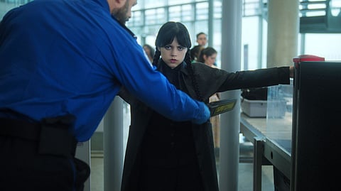Wednesday Addams is frisked by security at an airport in a scene from season 2 of 'Wednesday.'
