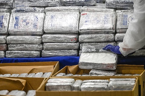 A gloved hand inspects tightly wrapped bricks of cocaine, stacked and boxed, seized by Portuguese authorities from banana shipments from Latin America, displayed at the Policia Judiciaria headquarters in Lisbon on 2 May 2023.