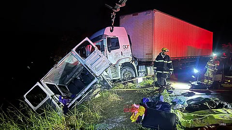 Firefighters work at the scene of a fatal head-on collision between a truck and a minivan on the BR-251 highway near Grao Mogol, Minas Gerais, Brazil, on 14 May 2025. The crash killed nine people and injured 10 others. Blankets, personal belongings, and emergency equipment are visible on the ground near the wreckage.