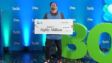Justin Simporios from Surrey, B.C. laughs joyfully while holding a giant $80 million Lotto Max cheque during a celebration event hosted by BCLC. The moment marks the largest individual lottery win in Canadian history.