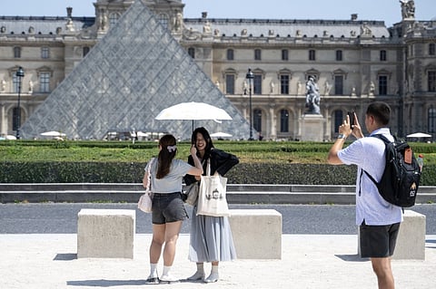 Young women protect themselves from the sun with an umbrella while they are being photographed in front of Louvre Pyramid designed by Chinese-US architect Ieoh Ming Pei during a warm afternoon in Paris, on June 13, 2025.
