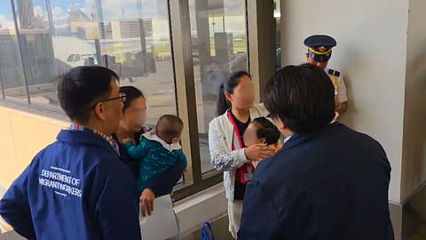 DMW Secretary Hans Cacdac and OWWA Chief Patricia Yvonne Caunan speak with two Filipino mothers and their children at the airport on Tuesday. The children had been undocumented in the UAE due to birth restrictions on children born out of wedlock.