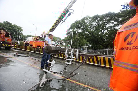 Personnel from Meralco, MMDA, and the Quezon City Police District work together to remove a fallen electric post along the northbound lane of Katipunan Avenue in Quezon City on Saturday, July 19, 2025. The post was knocked down by strong winds brought by the Habagat, intensified by Severe Tropical Storm Crising, around 11 a.m. Two vehicles reportedly crashed due to the incident.