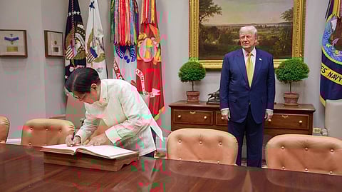 President Ferdinand Marcos Jr. logs at the White House while US President Donald Trump watches him.