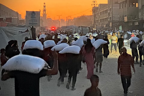 MEN walk carrying sacks of flour that were taken from a raided truck carrying foodstuffs, in Khan Yunis in the southern Gaza Strip on 22 July 2025.