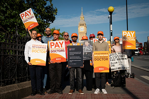 Protesters hold placards as they stand on a picket line outside St Thomas' Hospital, with in the background the Elizabeth Tower, commonly known by the name of the clock's bell "Big Ben", at the Palace of Westminster, home to the Houses of Parliament, in central London, on July 25, 2025. Hospital doctors in England will walk out for five days beginning July 25, ten months after they settled a long-running wave of strikes. The BMA doctors said the government had refused to negotiate on pay, "wanting to focus on non-pay elements without suggesting what these might be".