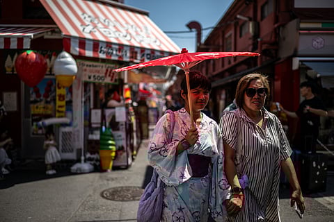 (FILES) Tourists share a traditional umbrella to shelter from the sun while walking along a shopping street at the Asakusa district near Sensoji Temple, on a hot day in Tokyo on July 28, 2025. Japan sweltered through its hottest July since records began in 1898, the weather agency has reported, warning of further "severe heat" in the month ahead. The average temperature in July was up a record 2.89C from the 1991-2020 average for the month, the Japan Meteorological Agency said on August 1.
