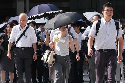 Commuters cross the street on their way to work on a hot, sunny morning in Tokyo on August 6, 2025.