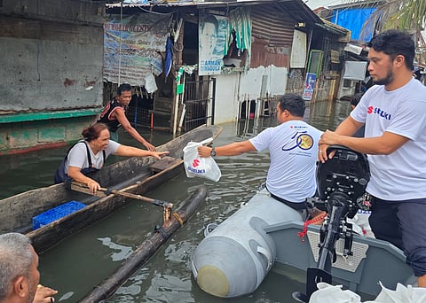 A Suzuki volunteer hands relief packs to residents stranded in chest-deep water.