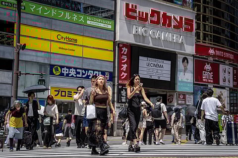 People cross a street in Tokyo on August 14, 2025.
