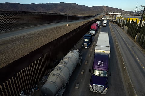 This aerial view shows cargo trucks queueing next to the border wall before crossing to the United States at Otay commercial port in Tijuana, Baja California state, Mexico on August 21, 2025. The US government announced on Thursday that it was suspending the issuance of visas to truck drivers, whom it accuses of “endangering the lives of Americans” on the roads.