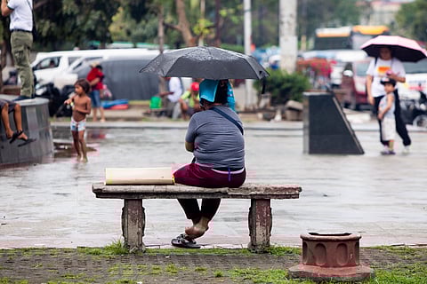A woman sits on bench at a park in Manila on Tuesday as she waits for the rain to subside. Class suspensions are also declared to several areas due to inclement weather.