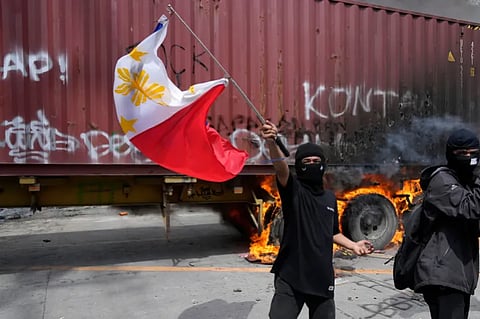 A protester waves a Philippine flag beside a burning truck in Manila after September protests took a violent turn. 