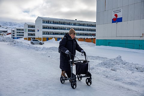 An elderly woman with a walking aid makes her way past a social housing estate in Nuuk, Greenland, on 6 March 2025.