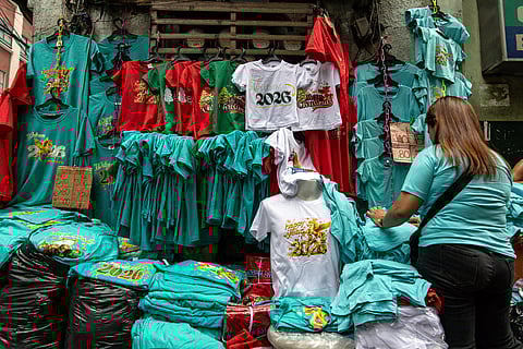 Shoppers buy New Year-themed T-shirts in Divisoria, Manila on Tuesday, 23 December 2025, a week before the New Year. 

Staff from printing shop Tatak Cayunda say the shirts sell for 140 pesos each.
