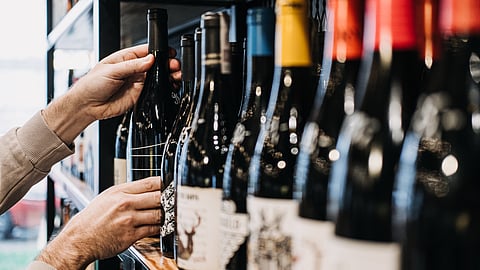 A shopper grips a wine bottle mid-aisle, the moment of choice crystallizing between habit, curiosity, and the promise of the night ahead.