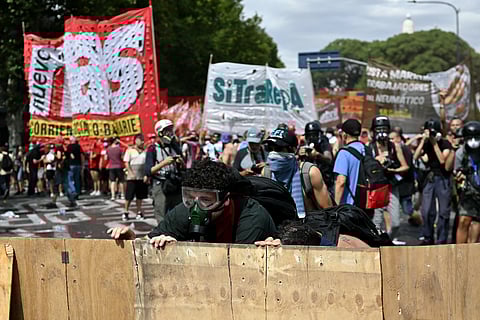 Demonstrators shield themselves while clashing with riot police during a protest called by trade unionists against the labor reform debate taking place in the National Congress in Buenos Aires on February 11, 2026. Argentine police fired tear gas and used water cannon on Wednesday to disperse demonstrators, who threw rocks and firebombs outside Congress during a Senate debate over radical labor reforms.