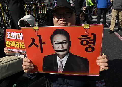 A protester holds a placard showing a photo of South Korea's impeached former president Yoon Suk Yeol reading "A death sentence" during a rally against Yoon near the Seoul Central District Court in Seoul on February 19, 2026. A South Korean court will rule on February 19, on insurrection charges against ex-president Yoon Suk Yeol, weighing whether he should be sentenced to death for his failed bid to impose military rule.

