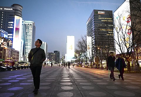 People walk in front of digital billboards at Gwanghwamun Square in Seoul on April 1, 2026. Hopes of making downtown Seoul dazzle more than Times Square have hit a setback with new guidelines to dim the massive digital billboards that light up the South Korean capital after a barrage of complaints.
