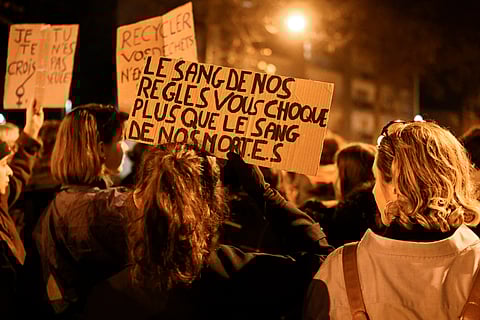  protestor holds a sign reading "The blood of our period shock you more than the blood of our dead" as people take part in a torchlight procession organised by "Nous Toutes" (All of Us), a French feminist collective, against sexist and violence to women, in Rennes, western France, on November 25, 2022, during the International Day for the Elimination of Violence Against Women.